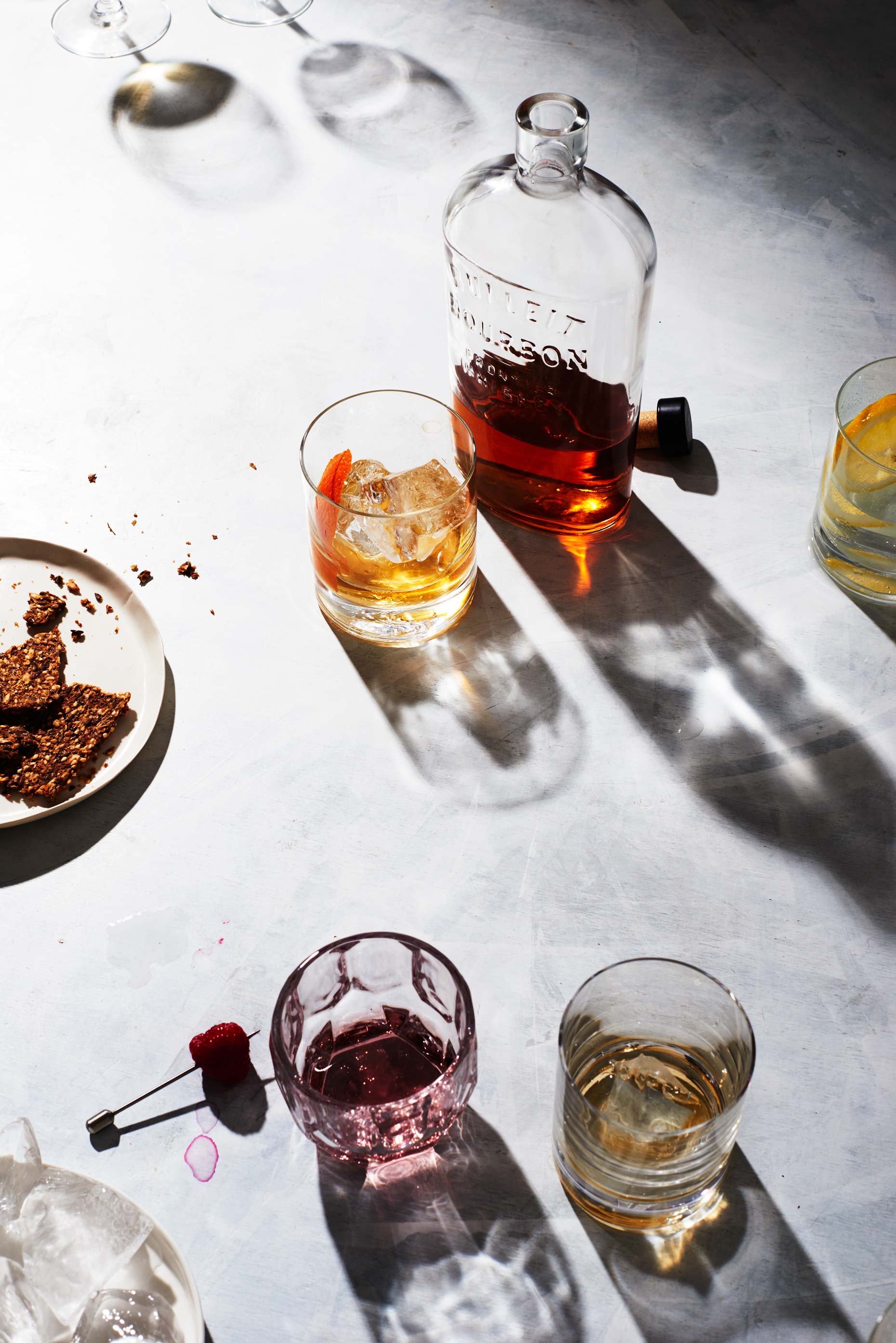 Glass of bourbon next to bottle and other drinks on white surface, photo by Food and Beverage Photographer Adrian Mueller, New York
