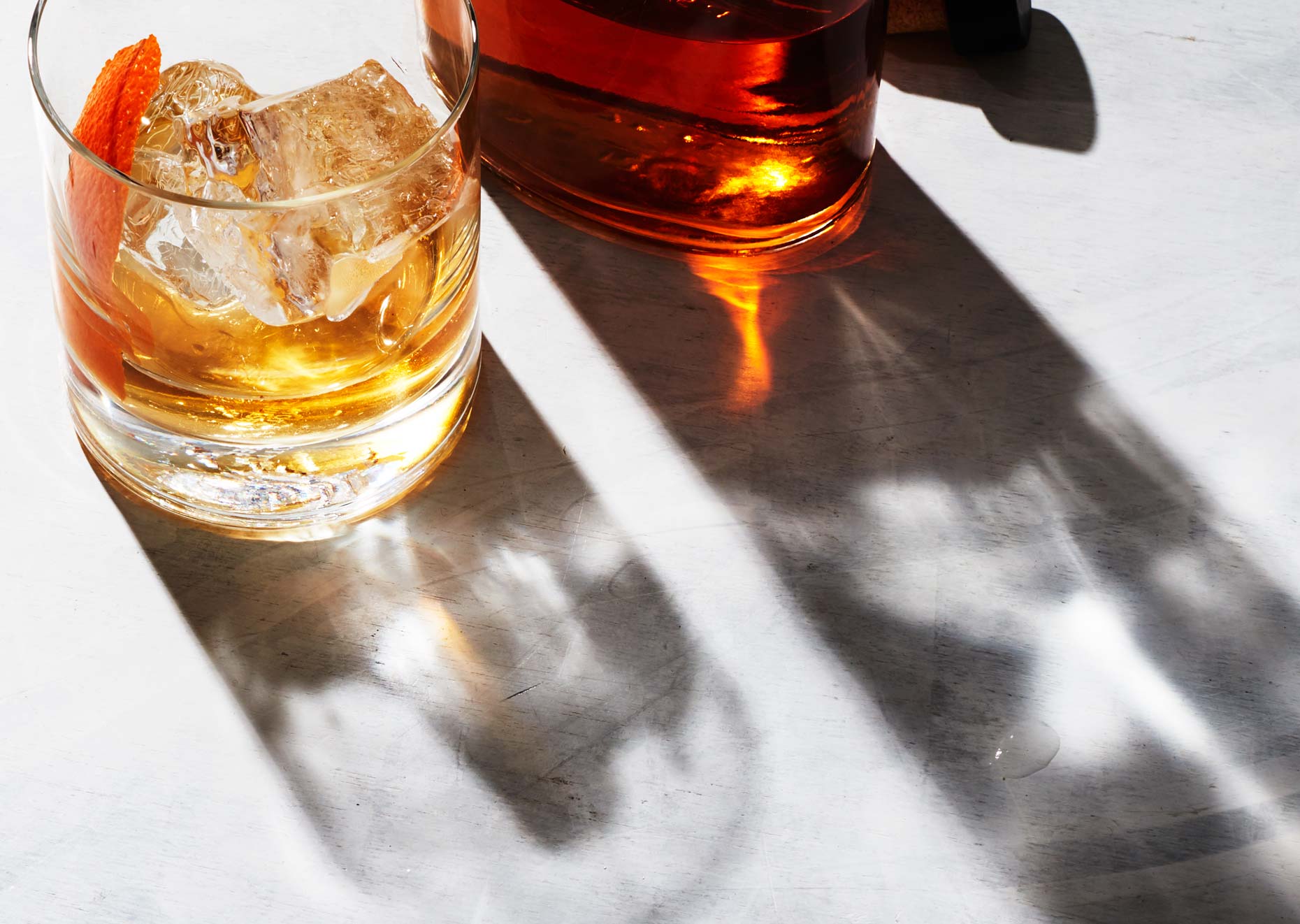 Glass of bourbon next to bottle on white surface, photo by Food and Beverage Photographer Adrian Mueller, New York
